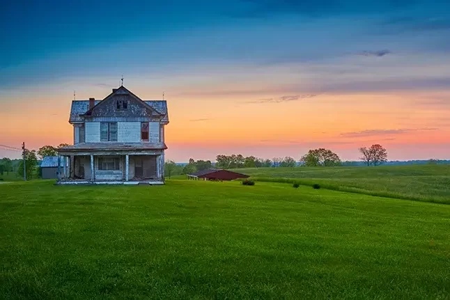 An image of an abandoned home with a a green cut lawn at dusk.