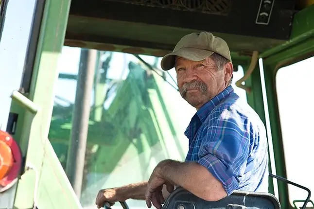 A man looking backward in a candid portrait of a farmer in a tractor.