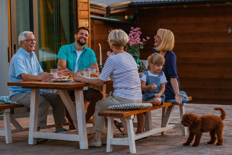 A family sitting down together for dinner outside at a picnic table while the adults talk and the child focuses on feeding a puppy.