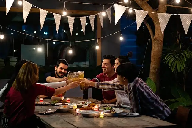 A group eating and tosting together at night with hanging lights and candles.