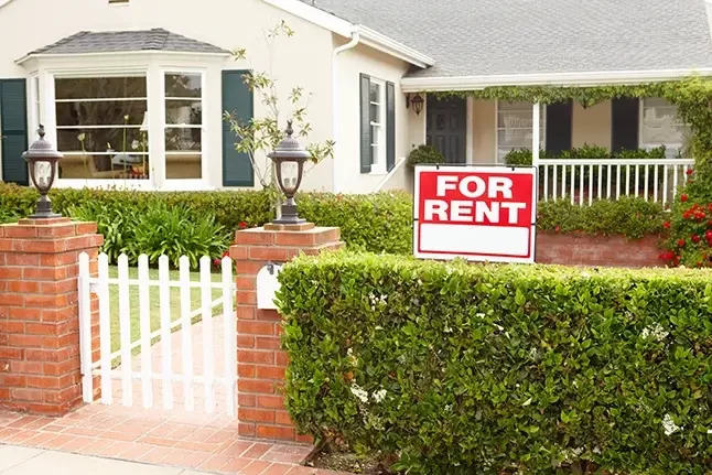 An image of a house for rent with a hedge and fence gate.